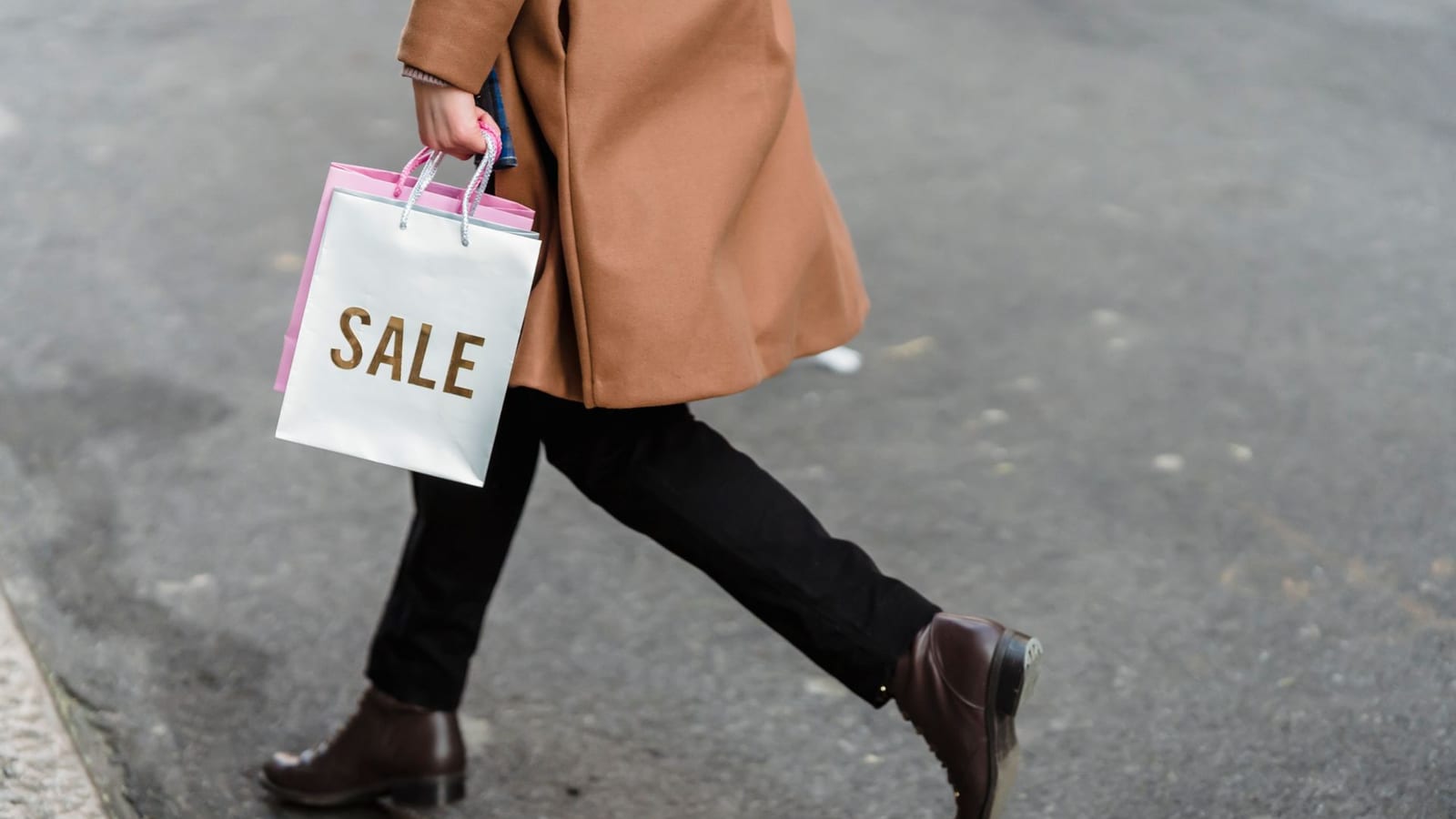 אדם במעיל הולך ברחוב עם שקית קניות שכתוב עליה SALE